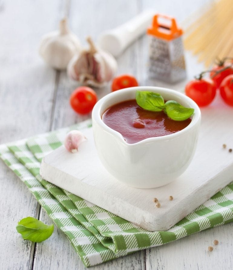 Fresh homemade tomato sauce in a white bowl on a white board, closeup, selective focus